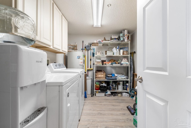 laundry room featuring cabinet space, light wood-style flooring, electric water heater, a textured ceiling, and washer and dryer