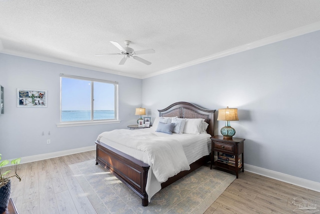 bedroom with a water view, ornamental molding, a textured ceiling, wood finished floors, and baseboards