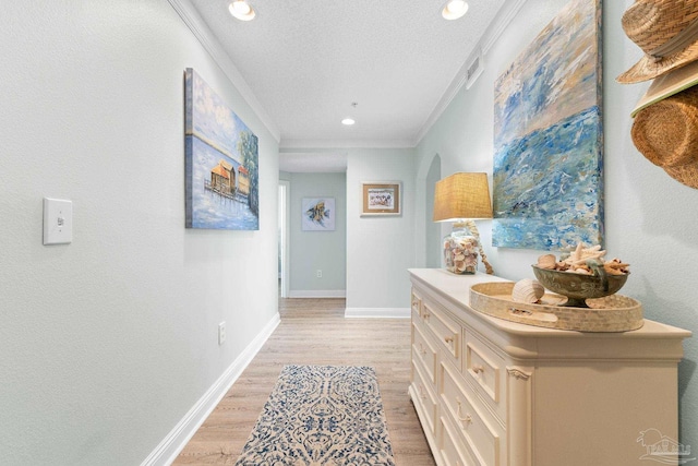 corridor featuring crown molding, light wood-style flooring, and a textured ceiling