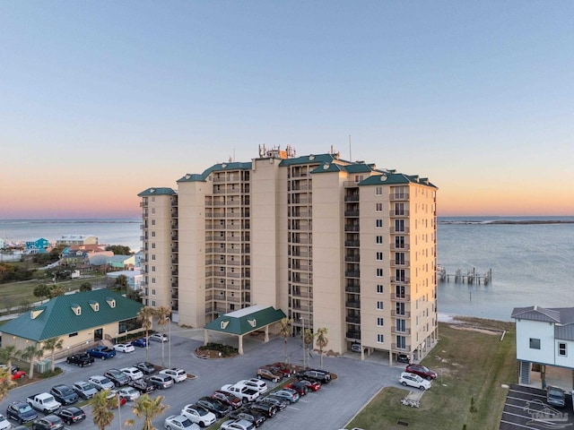 property at dusk with uncovered parking and a water view