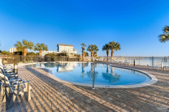 pool with a patio, a water view, and fence