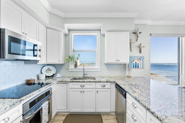 kitchen featuring a water view, appliances with stainless steel finishes, white cabinets, and a sink