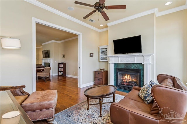 living room featuring a tile fireplace, wood finished floors, visible vents, baseboards, and ornamental molding