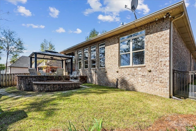 rear view of property featuring brick siding, fence, a lawn, and a gazebo