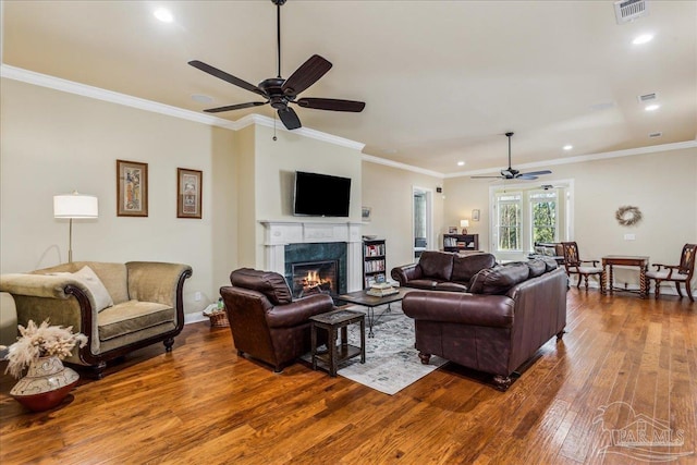 living area featuring ceiling fan, a high end fireplace, visible vents, ornamental molding, and wood-type flooring