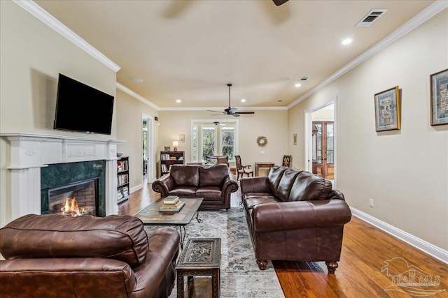 living room with wood finished floors, a high end fireplace, visible vents, baseboards, and crown molding