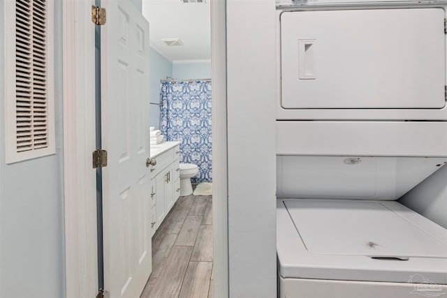 washroom with stacked washing maching and dryer, light hardwood / wood-style floors, and ornamental molding