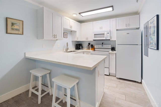 kitchen with a kitchen breakfast bar, white appliances, kitchen peninsula, sink, and white cabinets