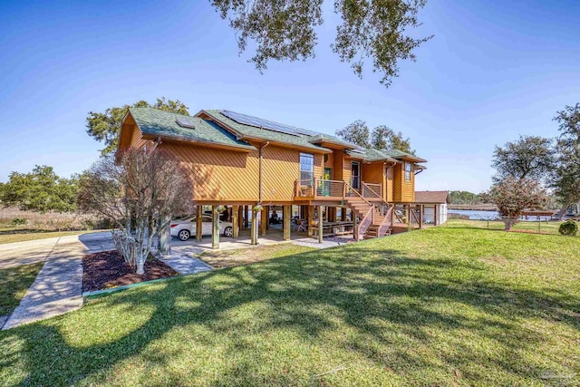 back of house with a yard, a shingled roof, and roof mounted solar panels