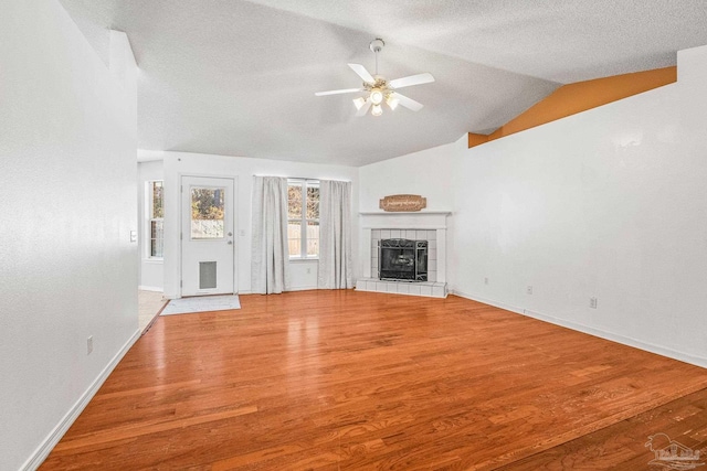 unfurnished living room featuring a tile fireplace, hardwood / wood-style floors, vaulted ceiling, and ceiling fan