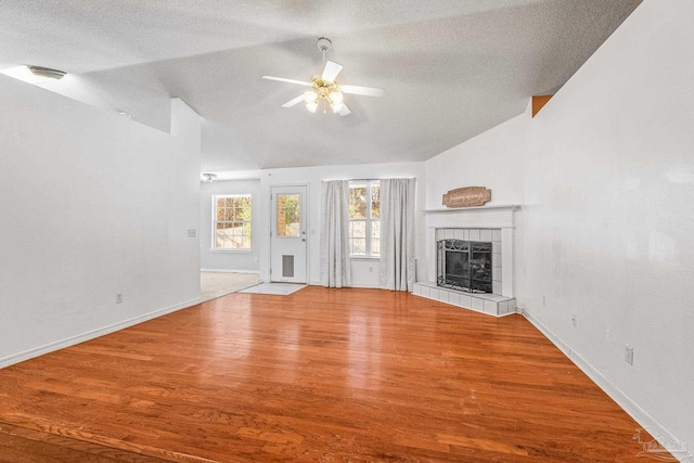 unfurnished living room with lofted ceiling, ceiling fan, a textured ceiling, wood-type flooring, and a tiled fireplace