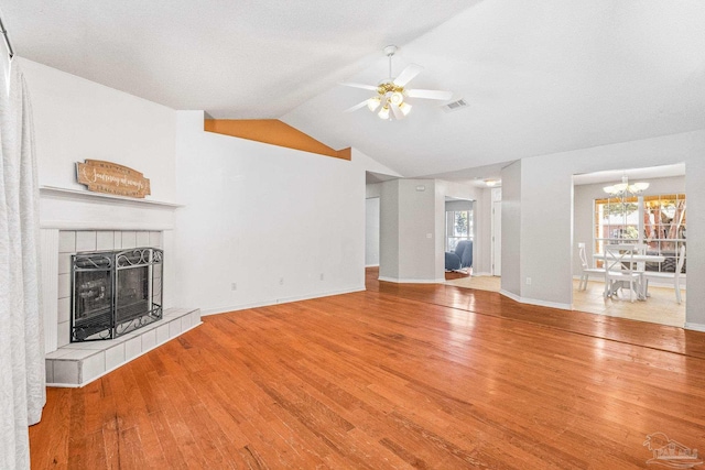 unfurnished living room with a tiled fireplace, lofted ceiling, hardwood / wood-style floors, and ceiling fan with notable chandelier