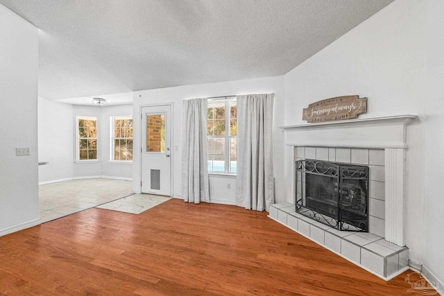 unfurnished living room with a tiled fireplace, wood-type flooring, and a textured ceiling