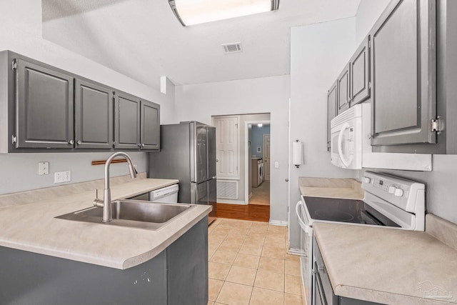 kitchen with kitchen peninsula, light tile patterned floors, white appliances, and gray cabinets