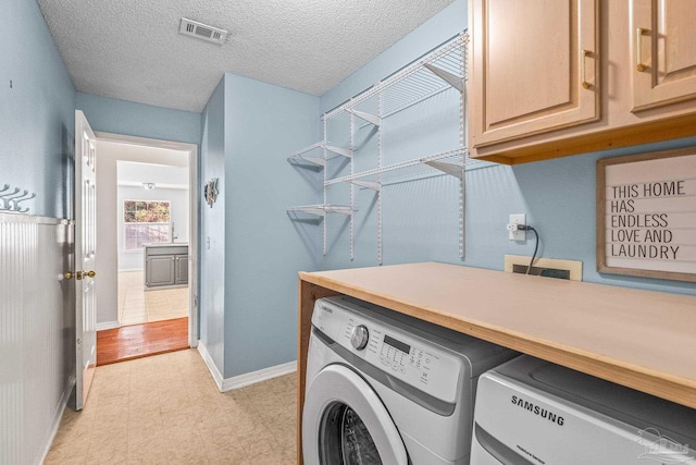 clothes washing area with separate washer and dryer, cabinets, and a textured ceiling