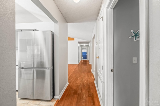 corridor featuring light wood-type flooring, a textured ceiling, and vaulted ceiling