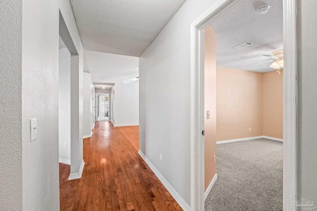 corridor with a textured ceiling and hardwood / wood-style flooring