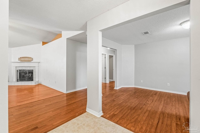 unfurnished living room featuring light hardwood / wood-style floors, a tiled fireplace, a textured ceiling, and vaulted ceiling