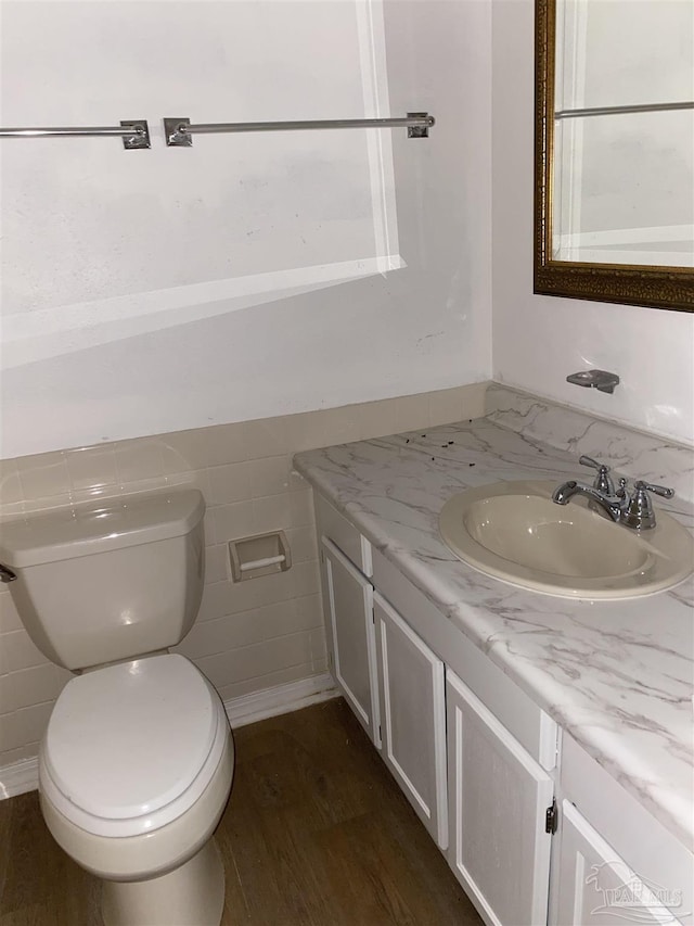 half bathroom with tile walls, vanity, toilet, and wood finished floors