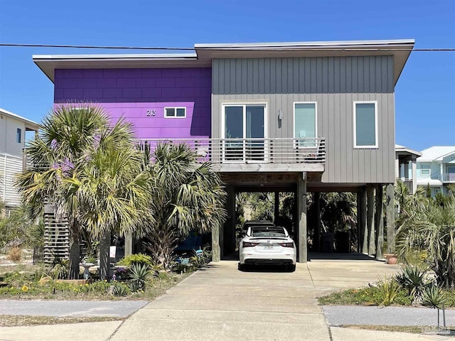 coastal home with board and batten siding, a balcony, a carport, and concrete driveway