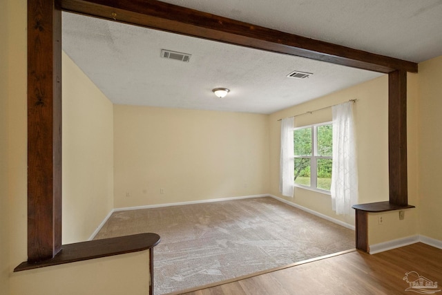 spare room featuring hardwood / wood-style floors, a textured ceiling, and beam ceiling