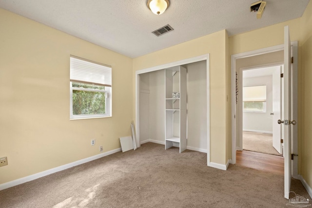 unfurnished bedroom with a textured ceiling, light carpet, and a closet