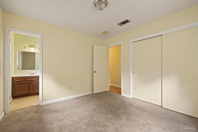 unfurnished bedroom featuring a closet, light colored carpet, and ensuite bath