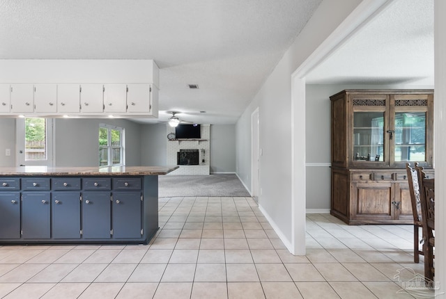 kitchen featuring ceiling fan, a fireplace, white cabinetry, and light tile patterned floors