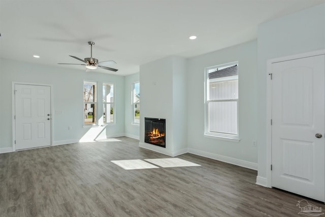 unfurnished living room featuring a glass covered fireplace, recessed lighting, baseboards, and wood finished floors