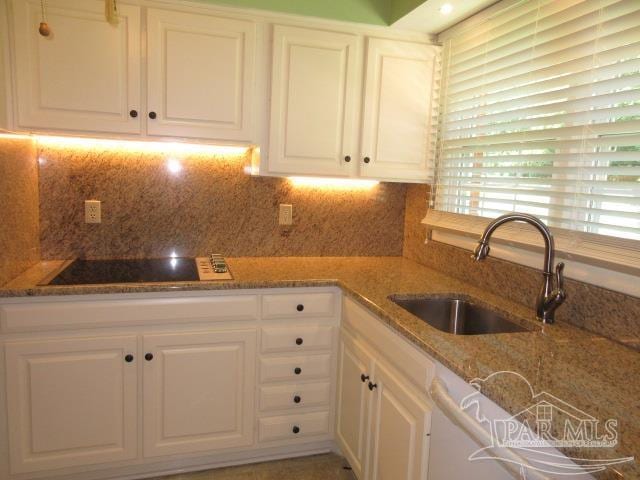 kitchen with stone countertops, white cabinets, sink, and black electric stovetop