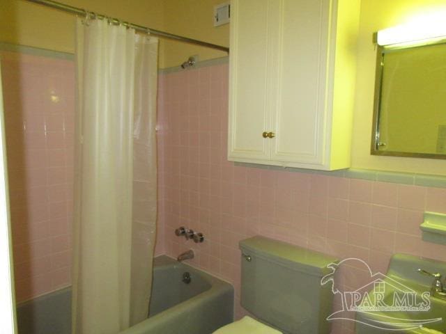 bathroom featuring tile walls, shower / bathtub combination with curtain, and toilet