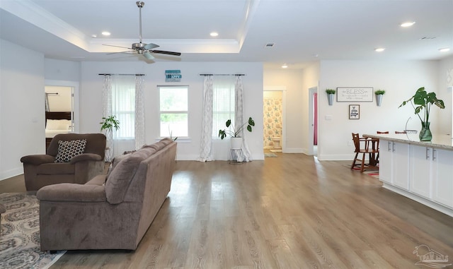 living room featuring ceiling fan, a tray ceiling, and light hardwood / wood-style floors