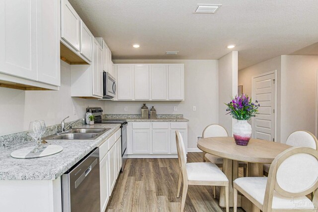 kitchen featuring appliances with stainless steel finishes, sink, white cabinets, a textured ceiling, and light hardwood / wood-style flooring