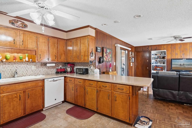 kitchen with dishwasher, sink, tasteful backsplash, kitchen peninsula, and wooden walls