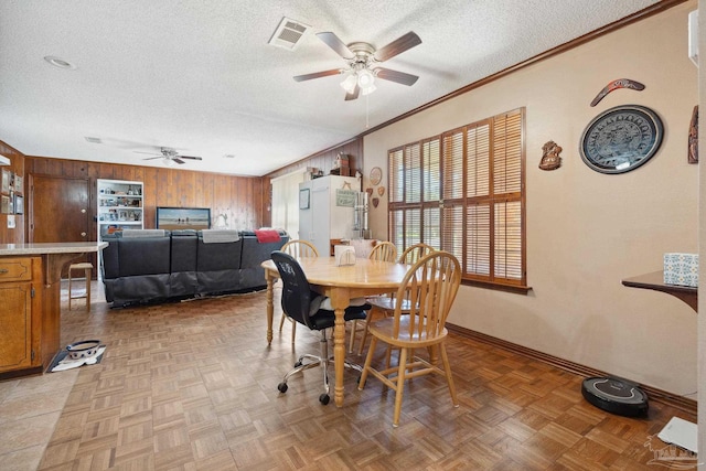 dining area featuring parquet flooring, a textured ceiling, ceiling fan, wooden walls, and crown molding