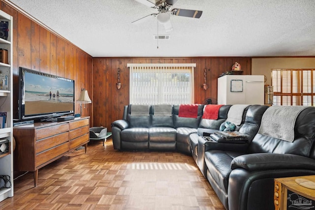 living room featuring ceiling fan, wood walls, crown molding, and a textured ceiling