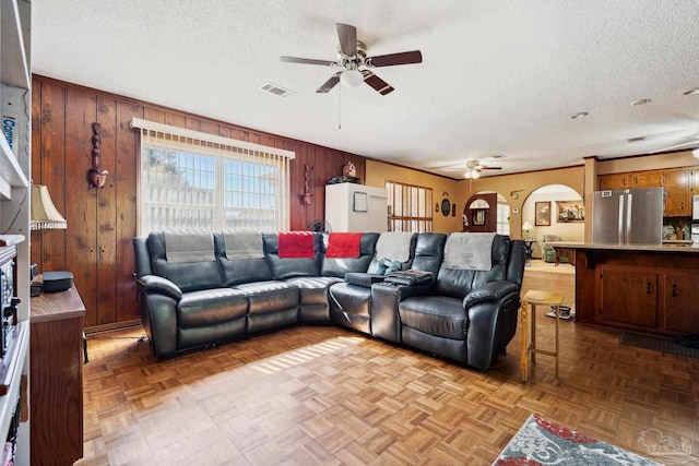 living room featuring ceiling fan, parquet floors, a textured ceiling, and wooden walls