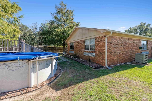 view of side of home featuring a covered pool, cooling unit, and a lawn