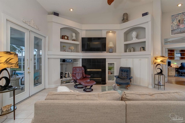 living room featuring a tiled fireplace, french doors, built in features, and light tile patterned floors