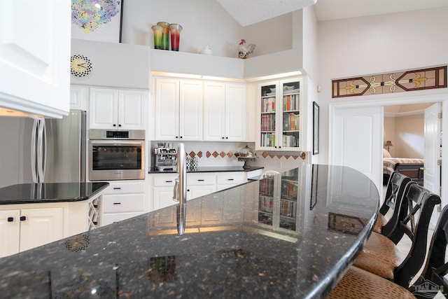 kitchen with white cabinetry, appliances with stainless steel finishes, high vaulted ceiling, a breakfast bar area, and dark stone countertops