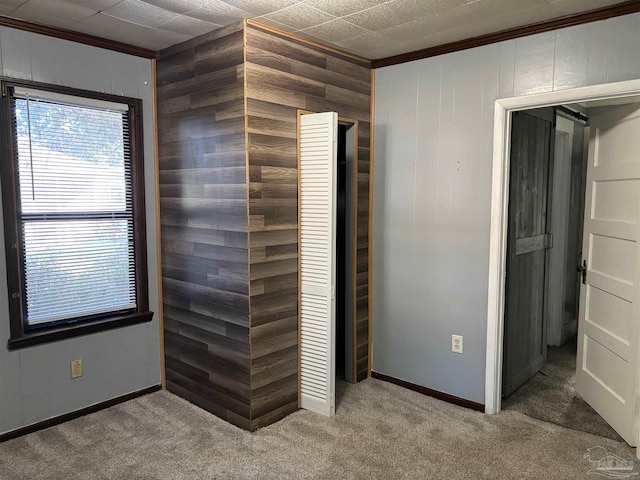 unfurnished bedroom with carpet flooring, crown molding, a closet, and wooden walls