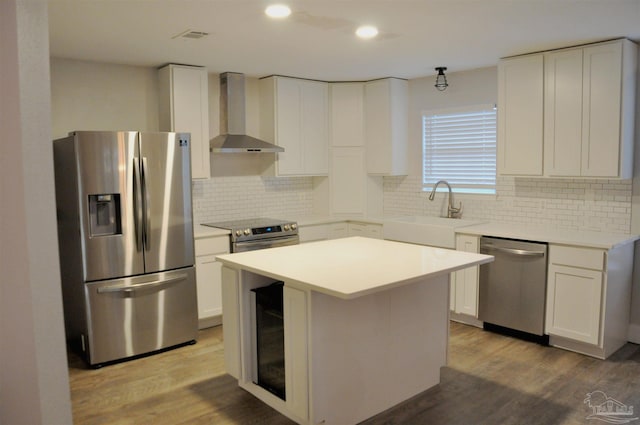 kitchen featuring a sink, light countertops, appliances with stainless steel finishes, wall chimney range hood, and a center island