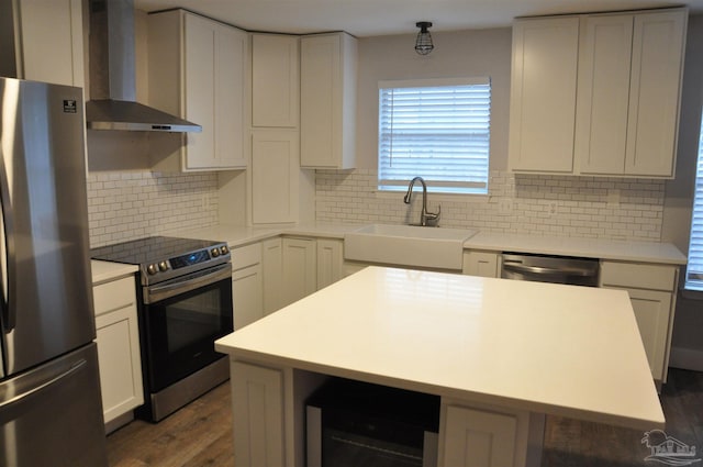 kitchen with stainless steel appliances, a sink, light countertops, a center island, and wall chimney exhaust hood