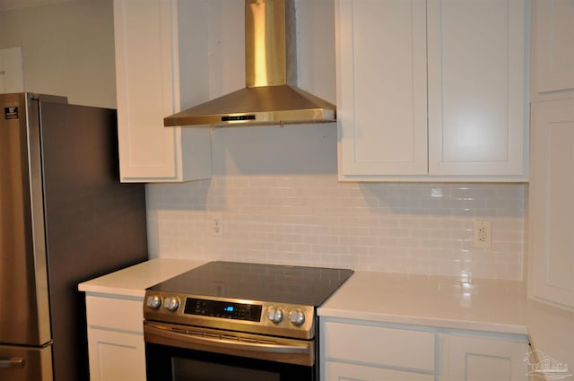 kitchen with light countertops, backsplash, appliances with stainless steel finishes, white cabinets, and wall chimney range hood