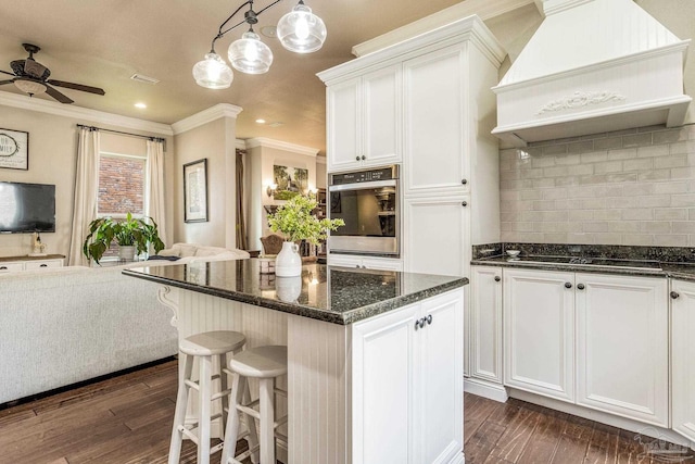 kitchen with white cabinets, oven, custom exhaust hood, hanging light fixtures, and black electric stovetop