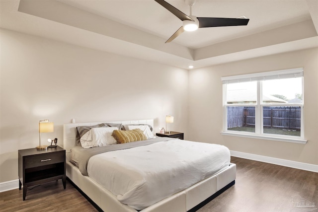 bedroom featuring a raised ceiling, ceiling fan, baseboards, and wood finished floors