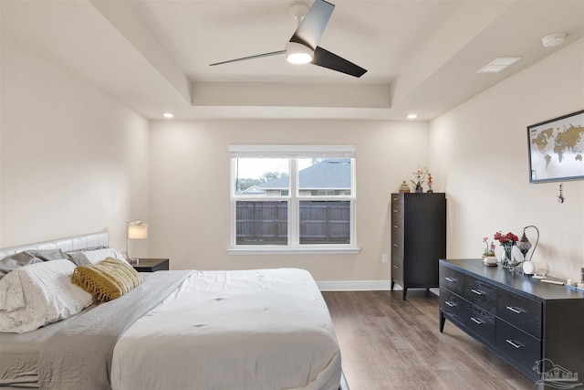 bedroom featuring baseboards, a tray ceiling, wood finished floors, and recessed lighting