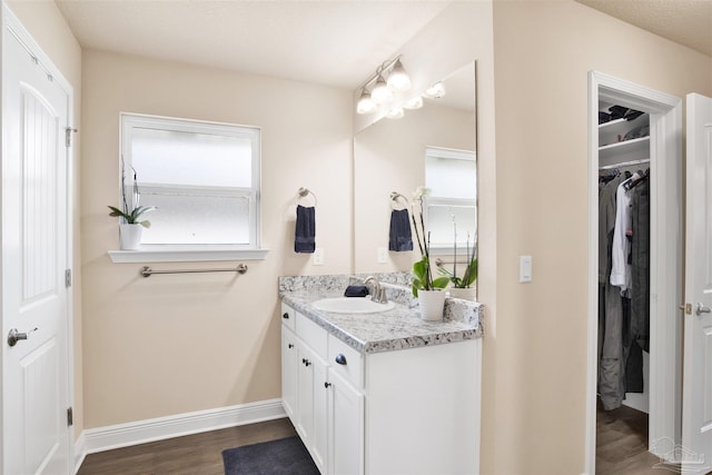 bathroom with a spacious closet, wood finished floors, vanity, and baseboards