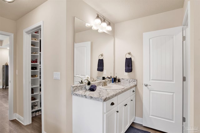 bathroom with a spacious closet, wood finished floors, vanity, and baseboards