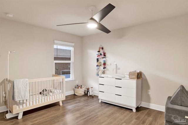 bedroom featuring ceiling fan, a crib, wood finished floors, and baseboards